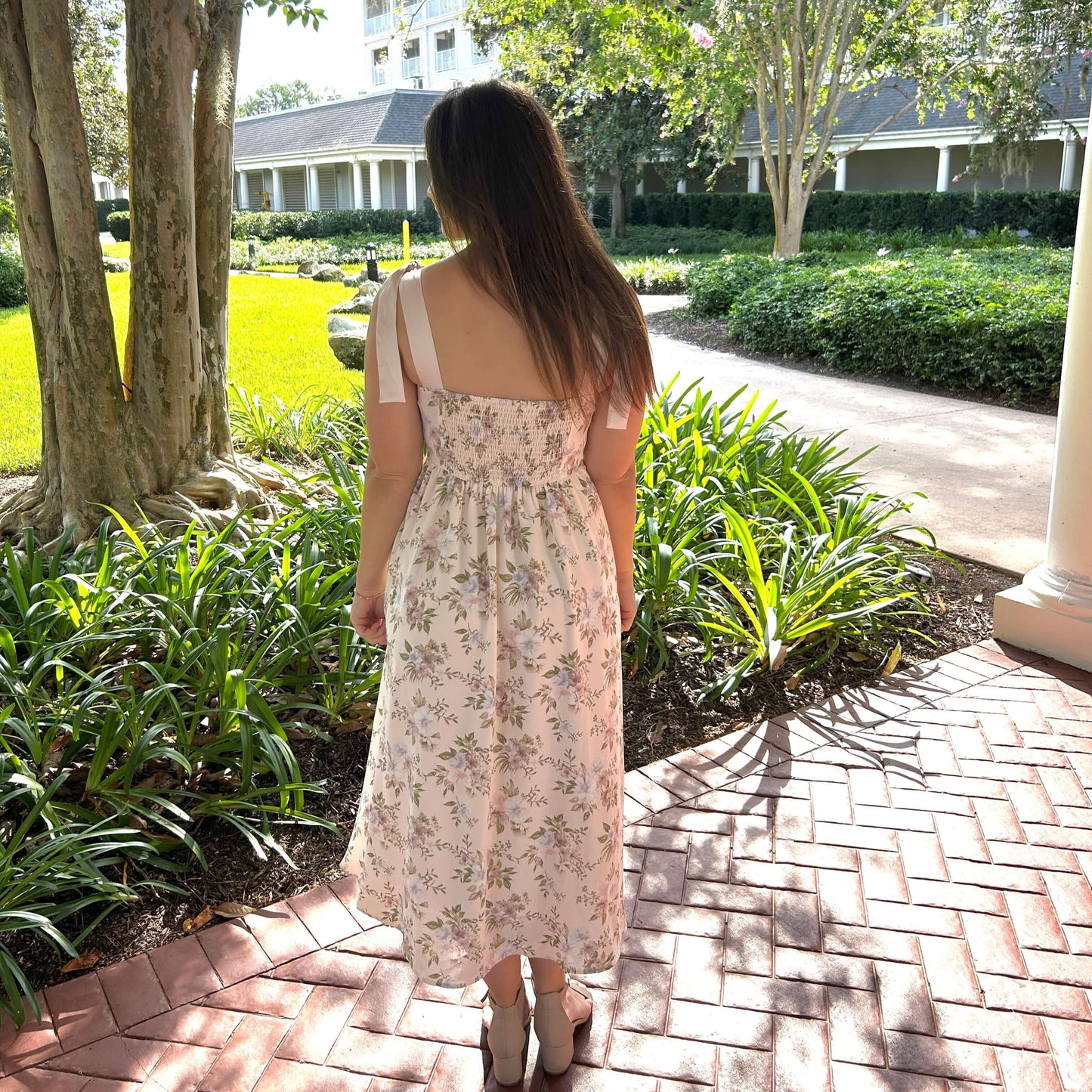 Woman in a floral dress walking on a brick path in a garden setting
