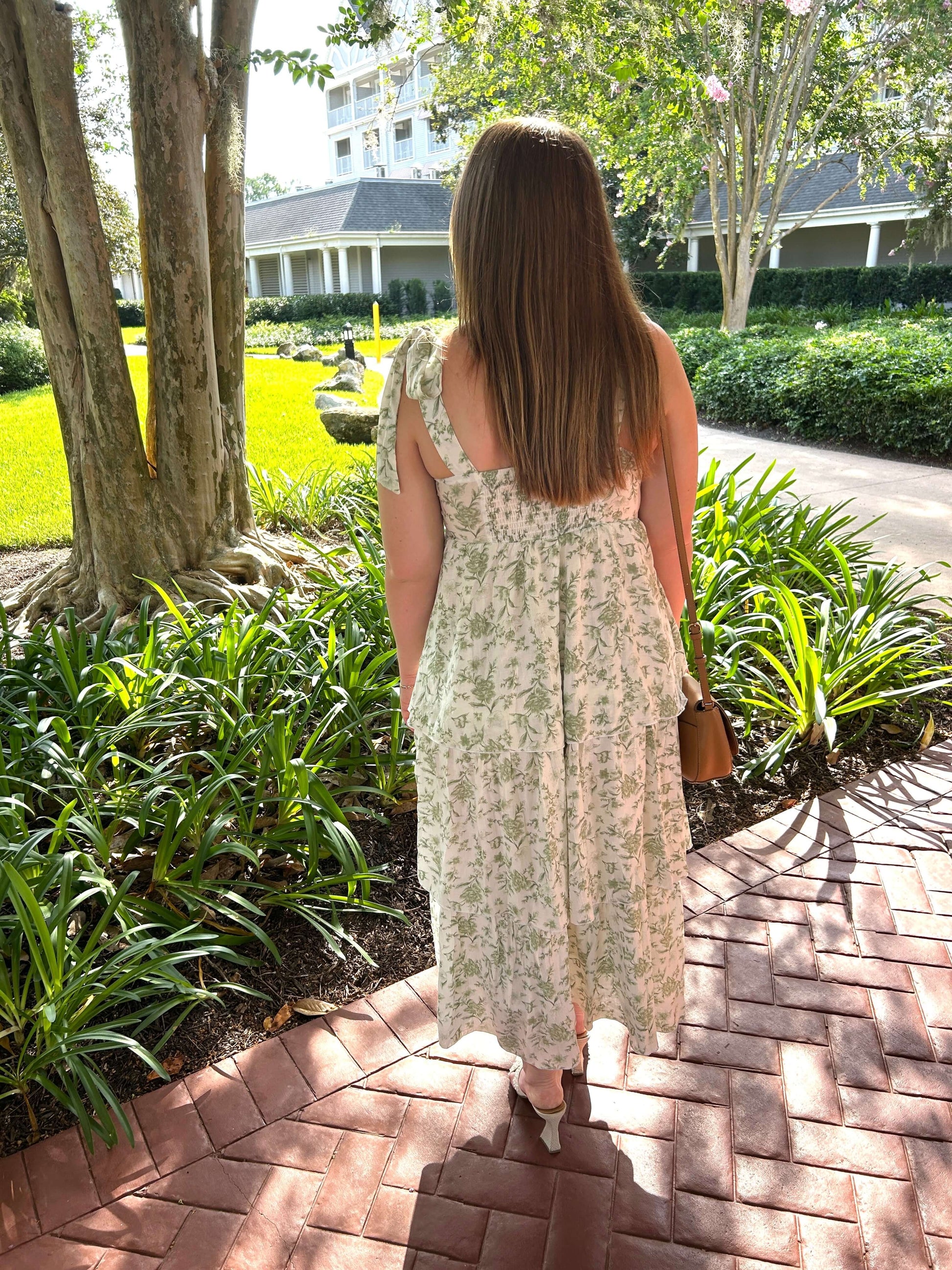 Woman in a floral dress walking on a brick path in a garden setting