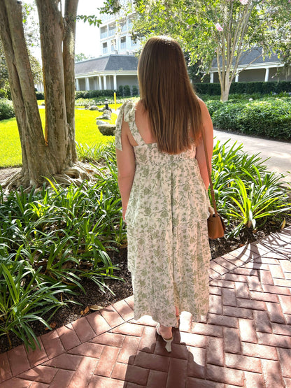 Woman in a floral dress walking on a brick path in a garden setting