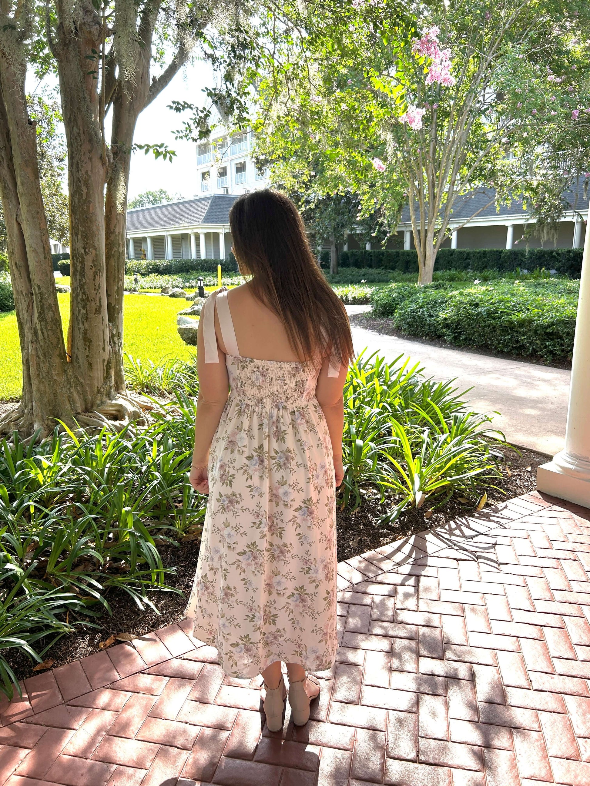 Woman in a floral dress walking on a brick path in a garden setting